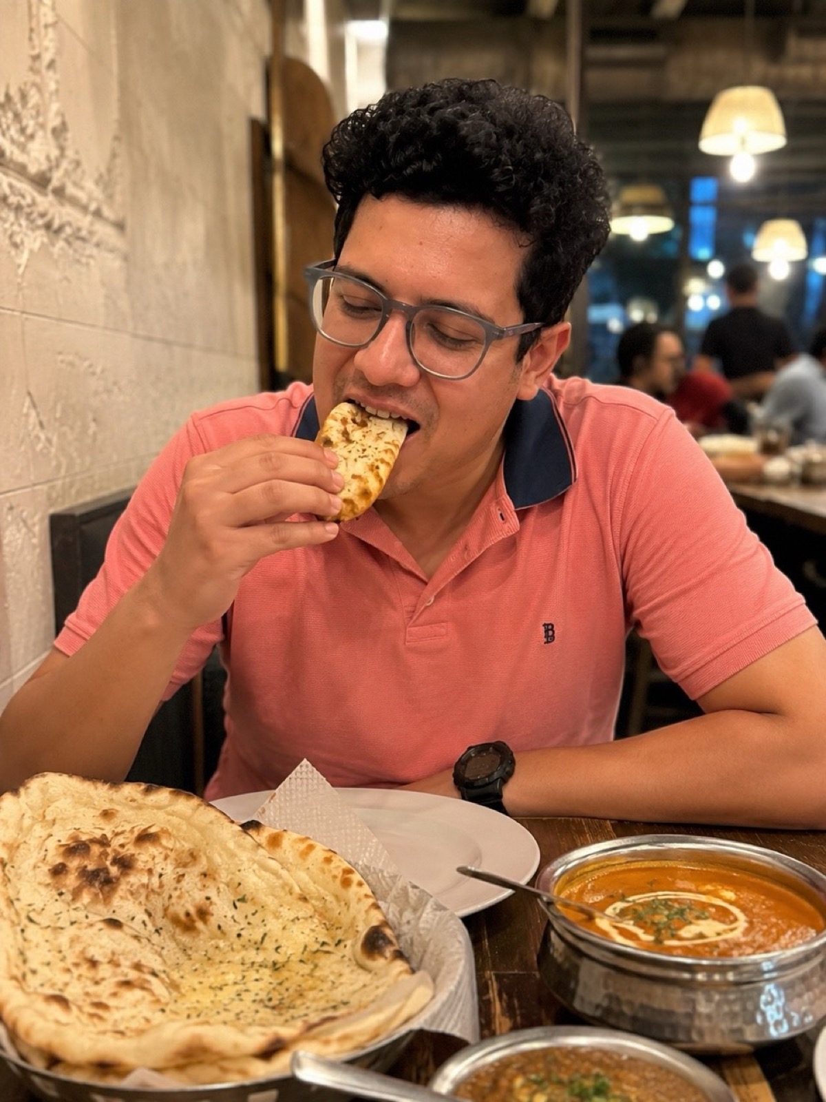 Abhijit eating naan at a restaurant table with naan and curry.